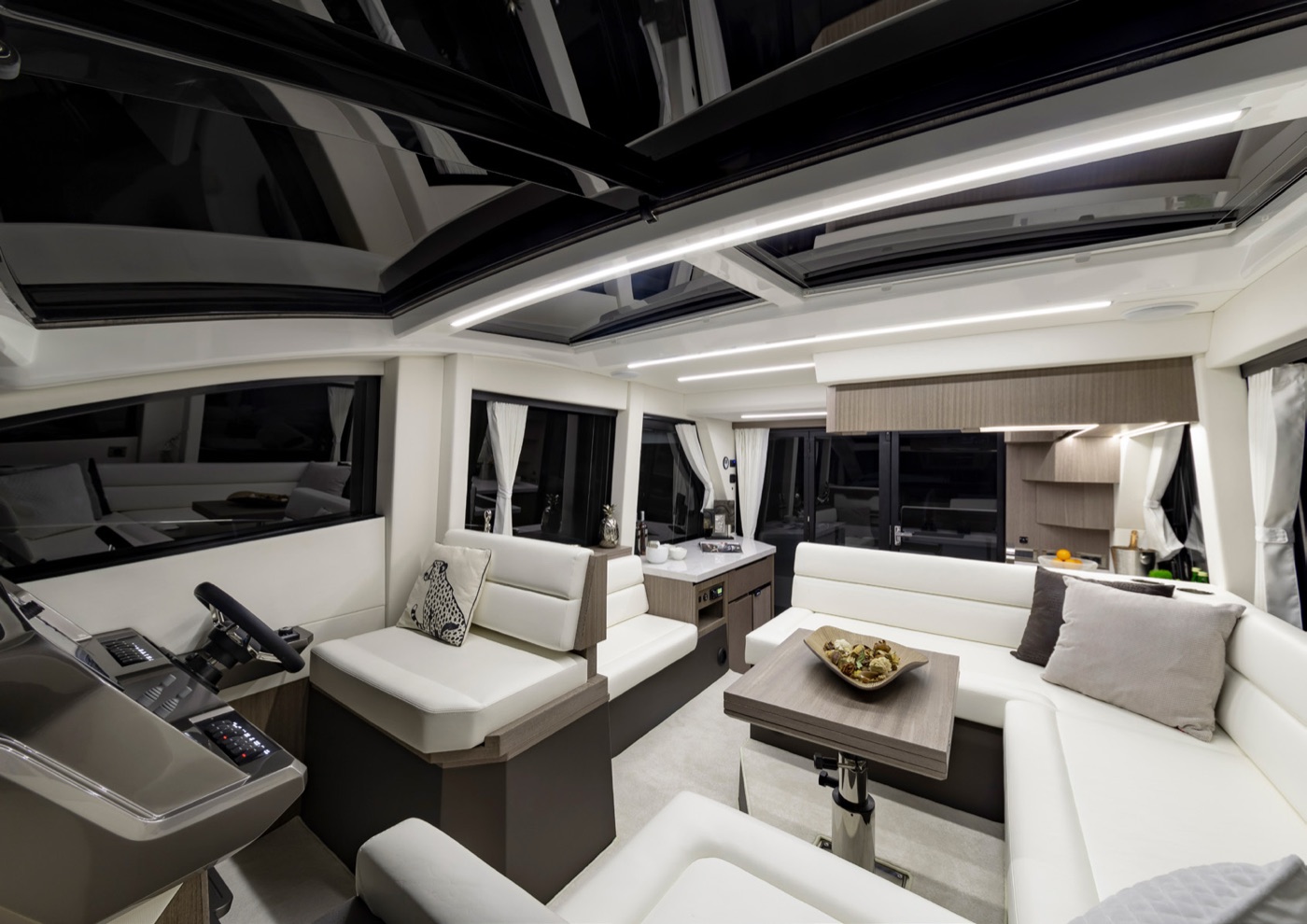 The saloon at night: white wraparound seating, helm station and open skylight
