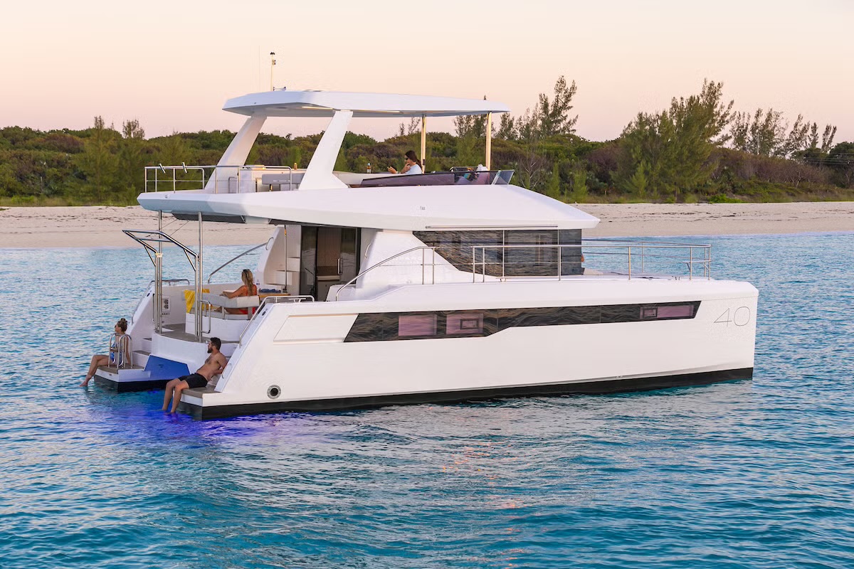 40PC anchored off a beach at dusk, guests on the swim platform