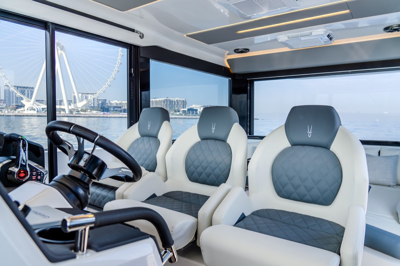 Quilted helm seats and wheel of the Oryx 47LX, waterfront city and observation wheel beyond the glazing