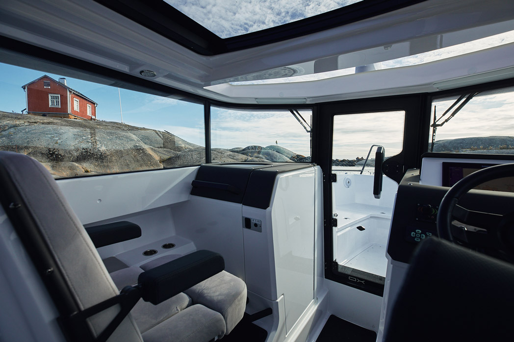 Helm and open roof hatch, with a Nordic archipelago cottage on the rocks outside